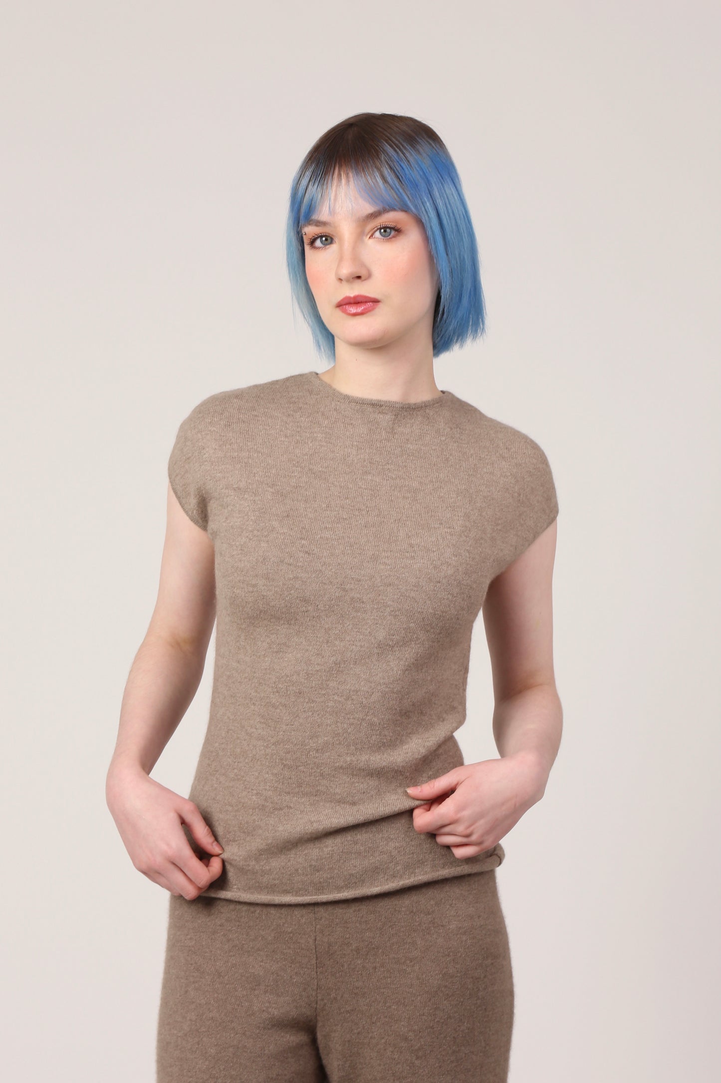 Our Little Tee in the colour brown is seen in the photo worn on a female model. It is paired with our trousers in brown. The tee is full length and falls around the waistline and it has a neckline that is almost halter like so little bit higher and fitted arm holes, creating a flattering feminine shape on the body.